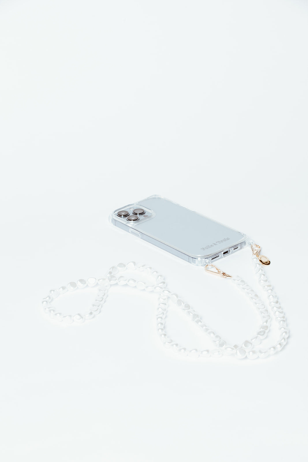 Clear phone case with the Long Pearl Phone Cord of white baroque pearls looped beside it on a white background.