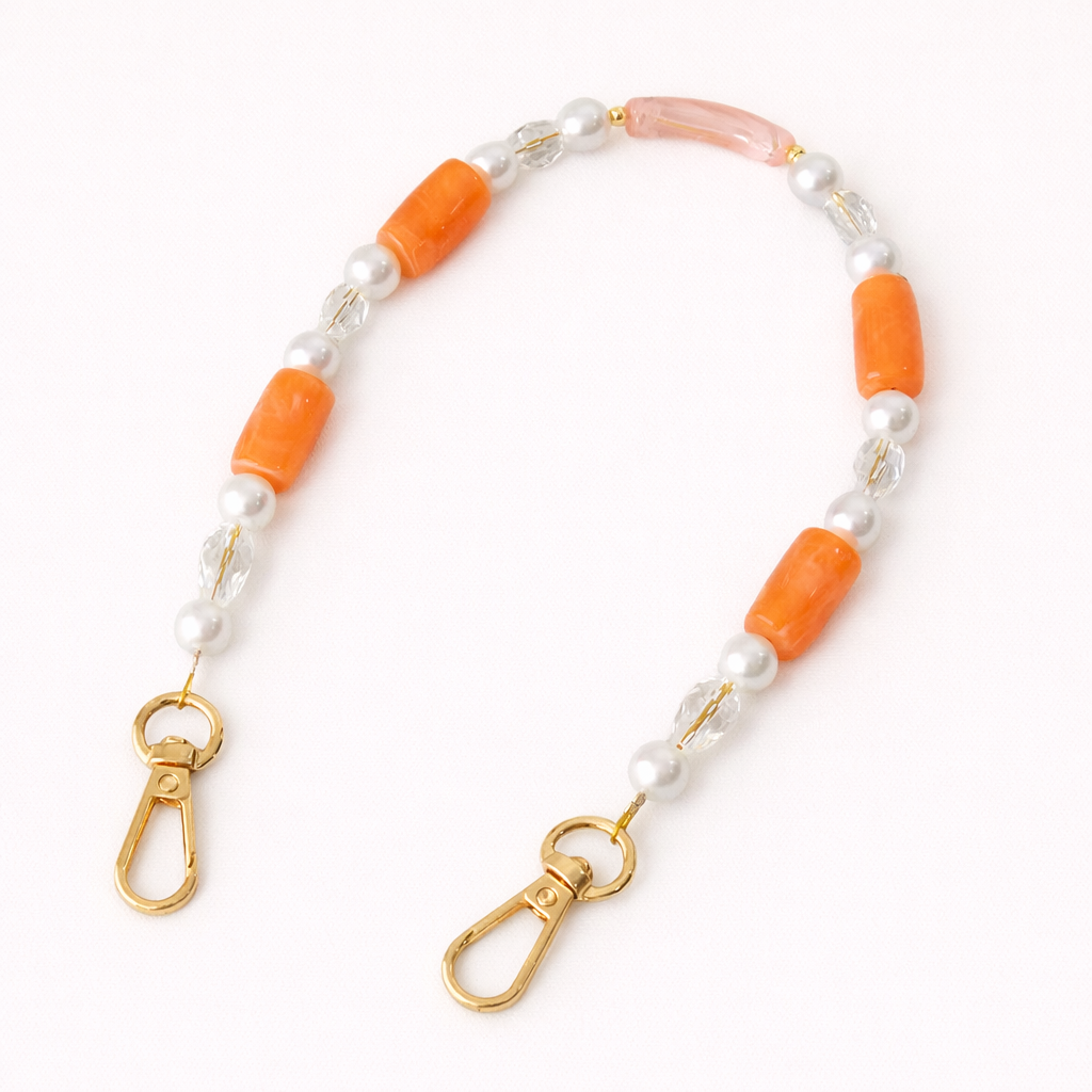 Coral beaded Loreto short phone strap coiled flat, accented with pearls, crystals, and gold-tone clasps.