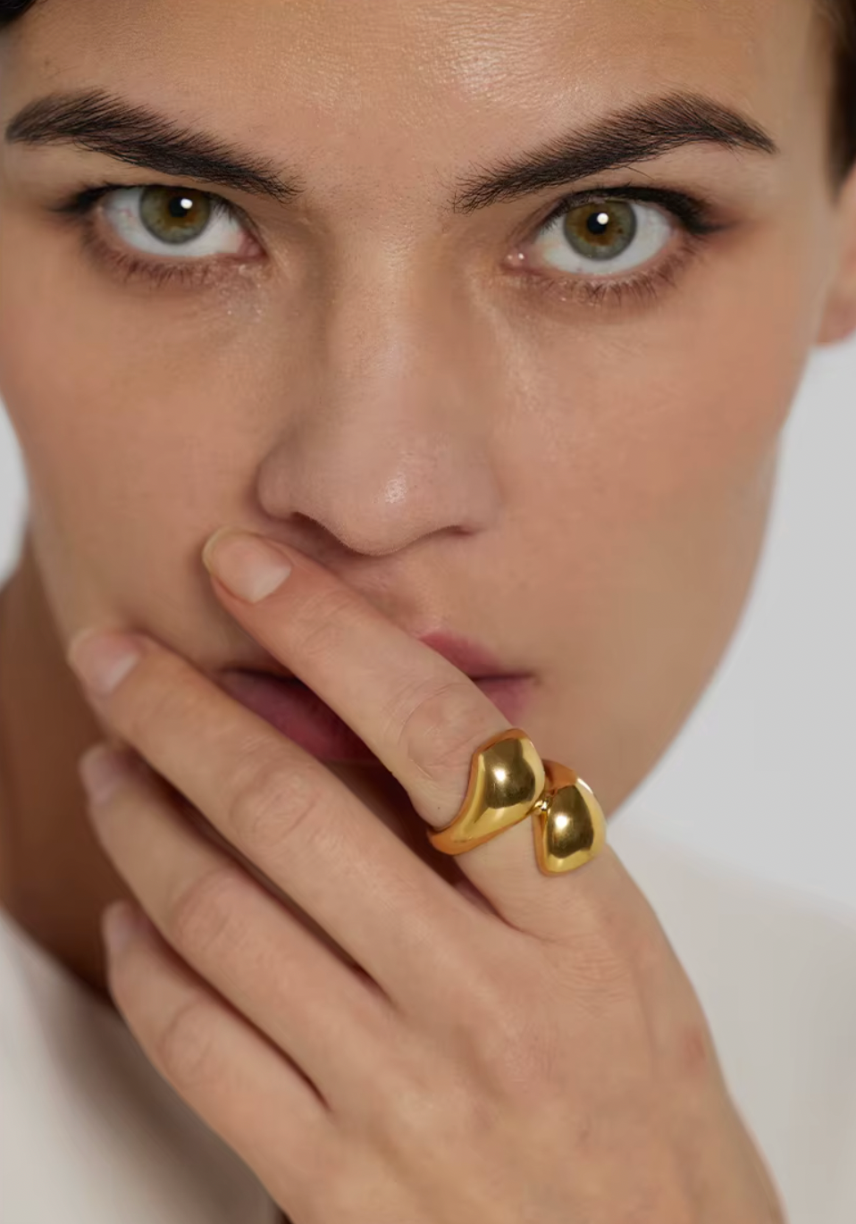 Model touches her lips wearing the gold Lunaire RING, its two overlapping domes visible in close-up.