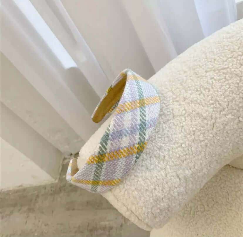 A single lavender, mustard and green plaid padded headband resting on a cream boucle chair.