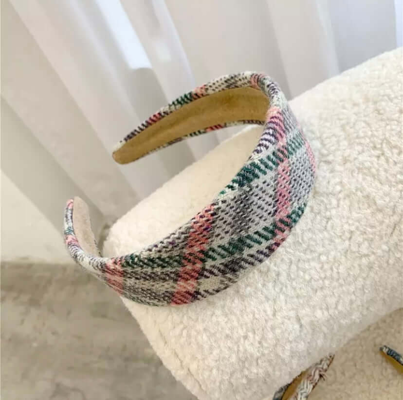 A single pink, green and cream plaid padded headband resting on a cream boucle chair.