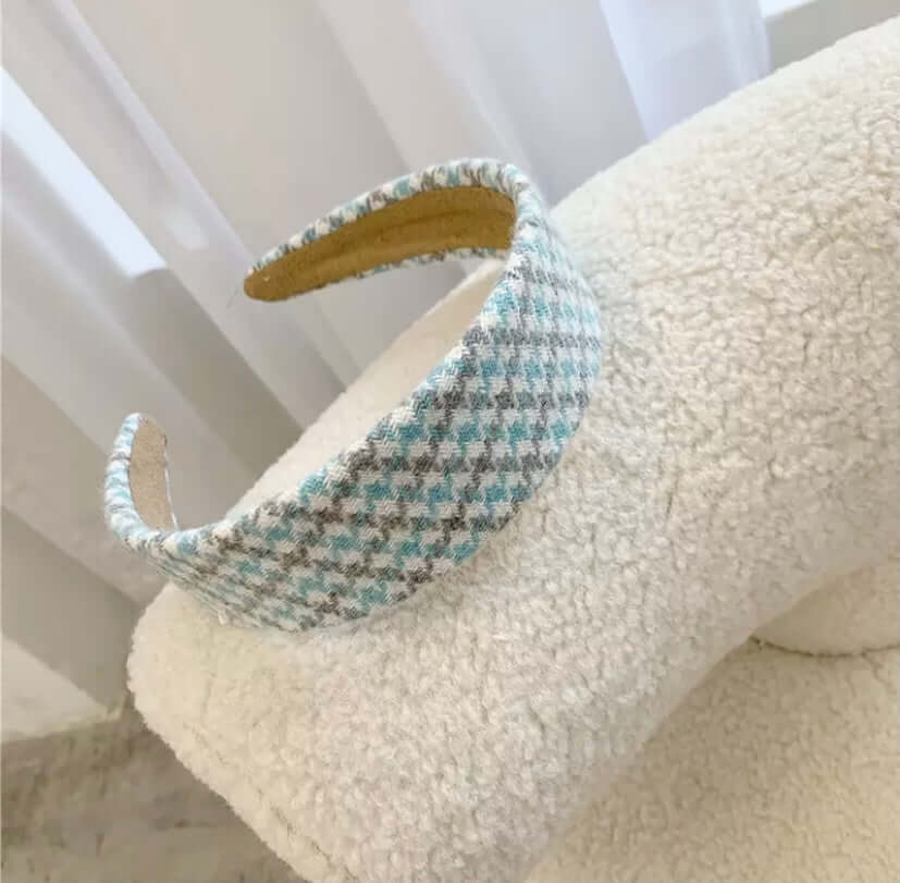 A single blue and grey houndstooth check padded headband resting on a cream boucle chair.