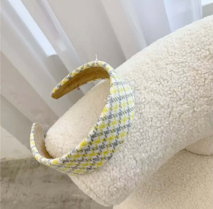 A single yellow and grey houndstooth check padded headband resting on a cream boucle chair.
