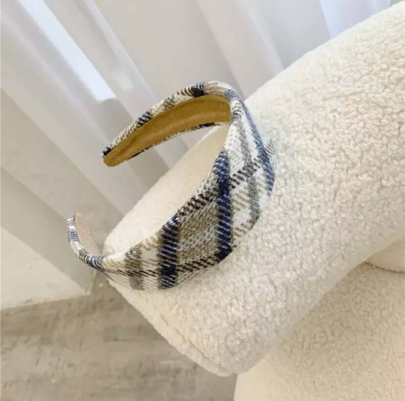 A single navy, tan and cream plaid padded headband resting on a cream boucle chair.