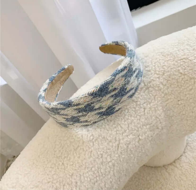 A single blue and cream houndstooth check padded headband resting on a cream boucle chair.