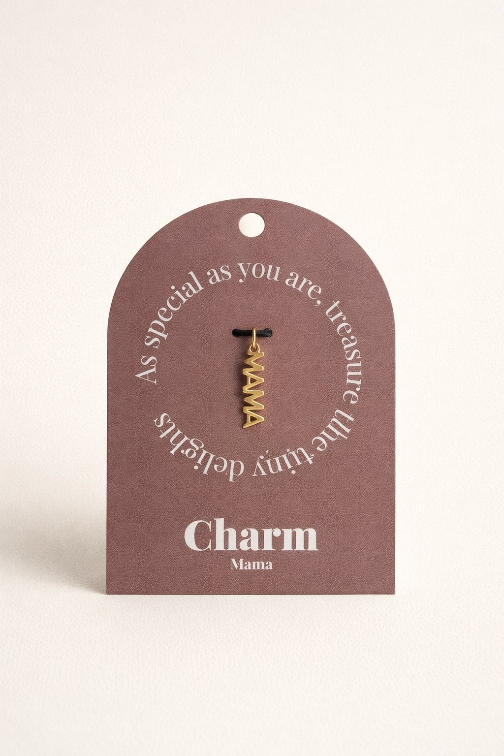 The Mama CHARM displayed on a mauve Charm gift tag, the gold vertical MAMA pendant hanging from a black cord.