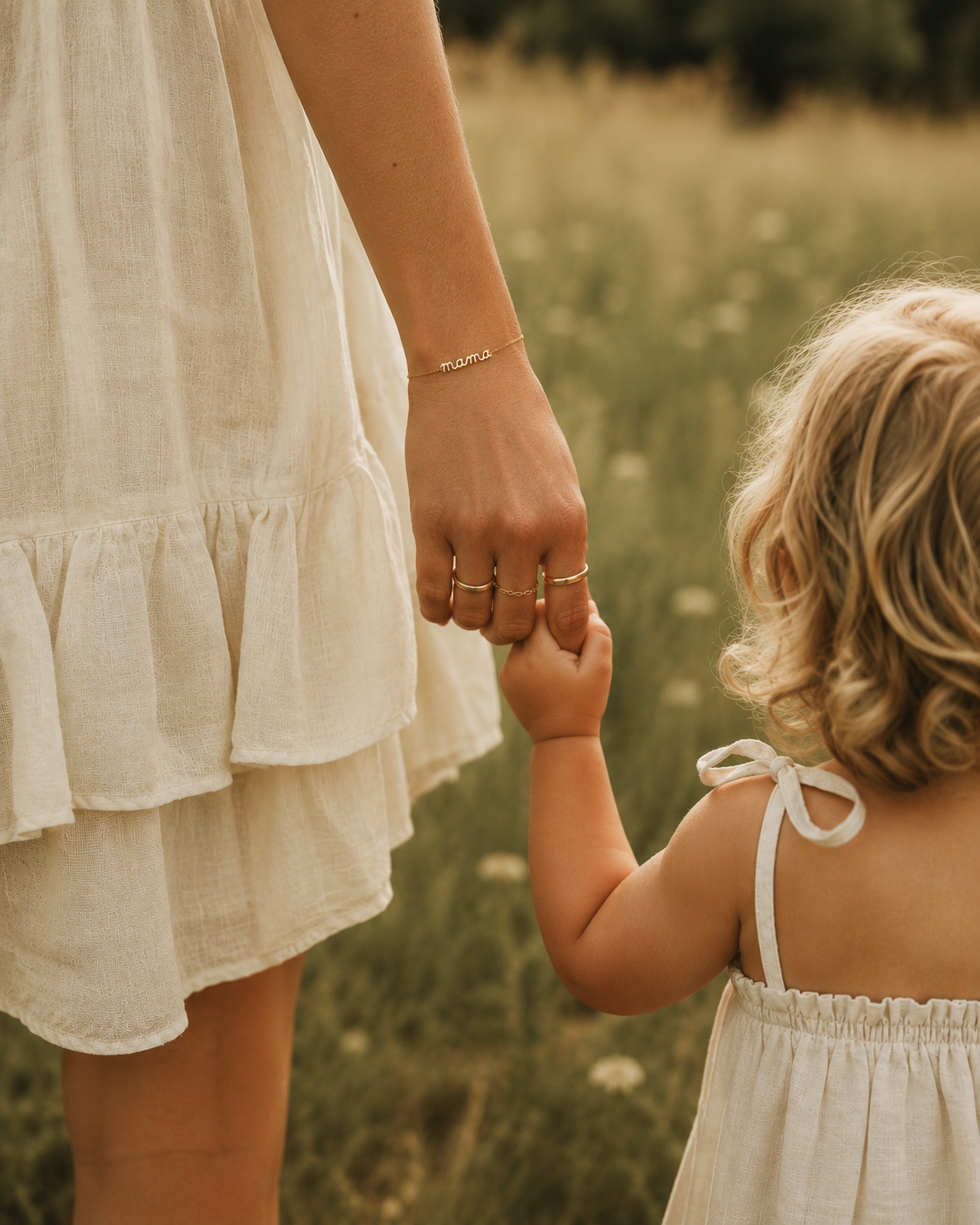 The Folie à Trois Mama Small BRACELET and stacked gold rings on a mother's wrist as she holds her toddler's hand in a wildflower field.