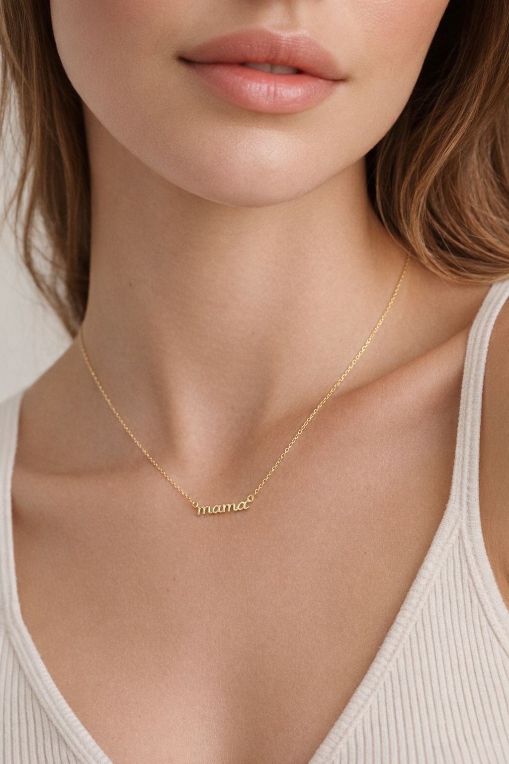 The Mama Small NECKLACE in gold worn at the neckline, the script mama pendant resting above a cream ribbed tank top.