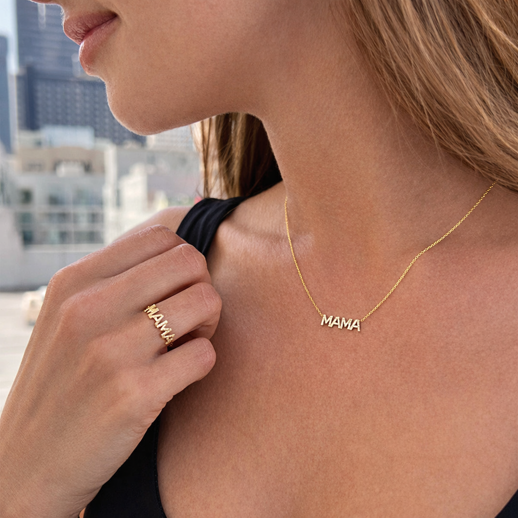 The Mama Zirconia NECKLACE worn outdoors with a matching MAMA ring, the gold pendant catching light against a city view.