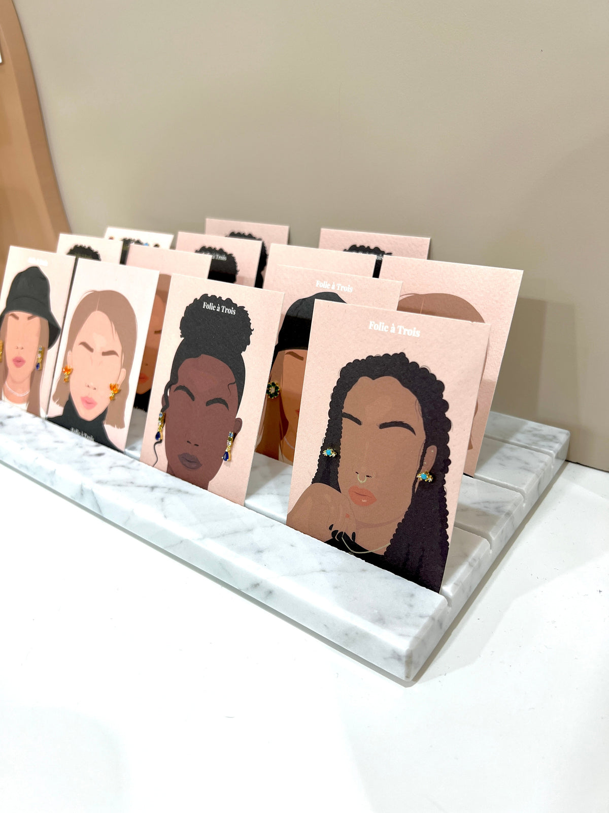 Marble Tray DISPLAY with a front lip holding illustrated Folie à Trois earring cards upright on a white shelf.
