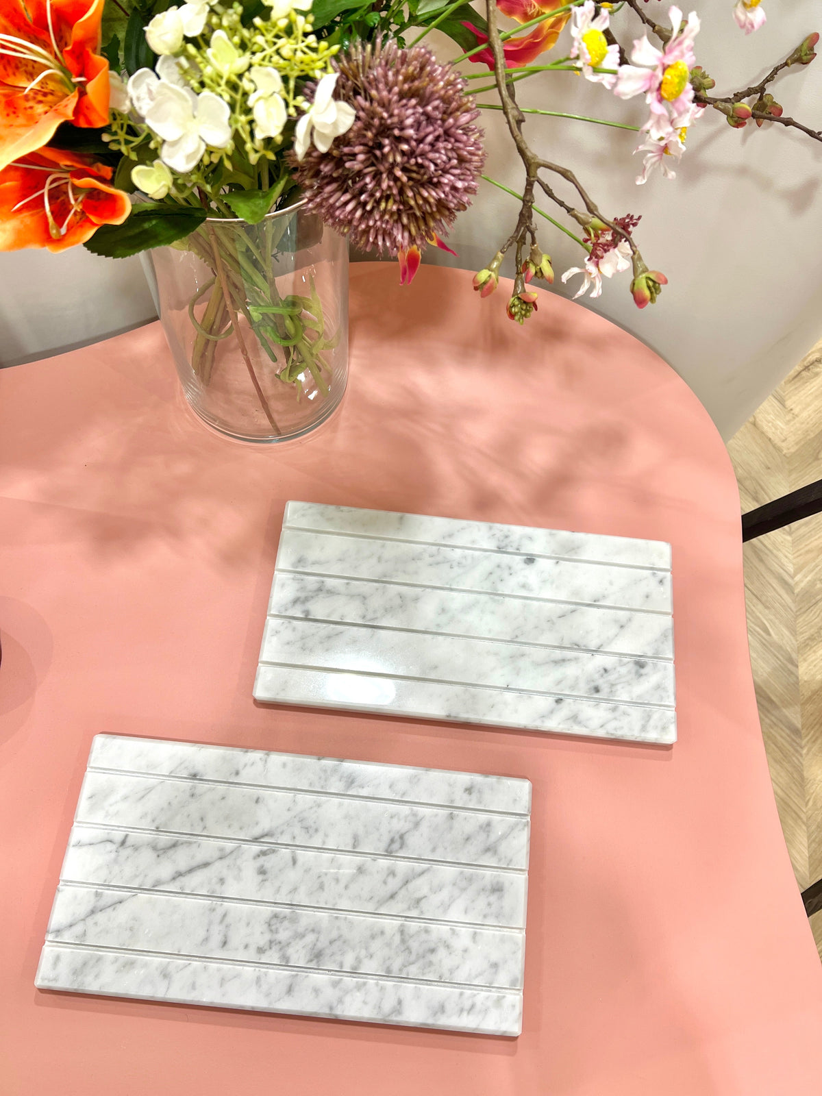 Two white Marble Tray DISPLAY slabs with grooved card slots on a pink table beside a vase of colorful fresh flowers.