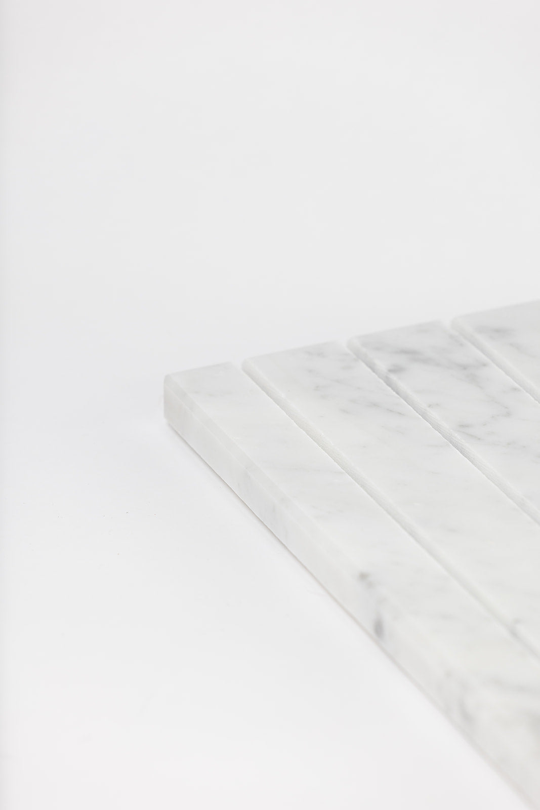 Close-up of a Marble Tray DISPLAY corner showing grooved slots cut into white marble with soft grey veining.
