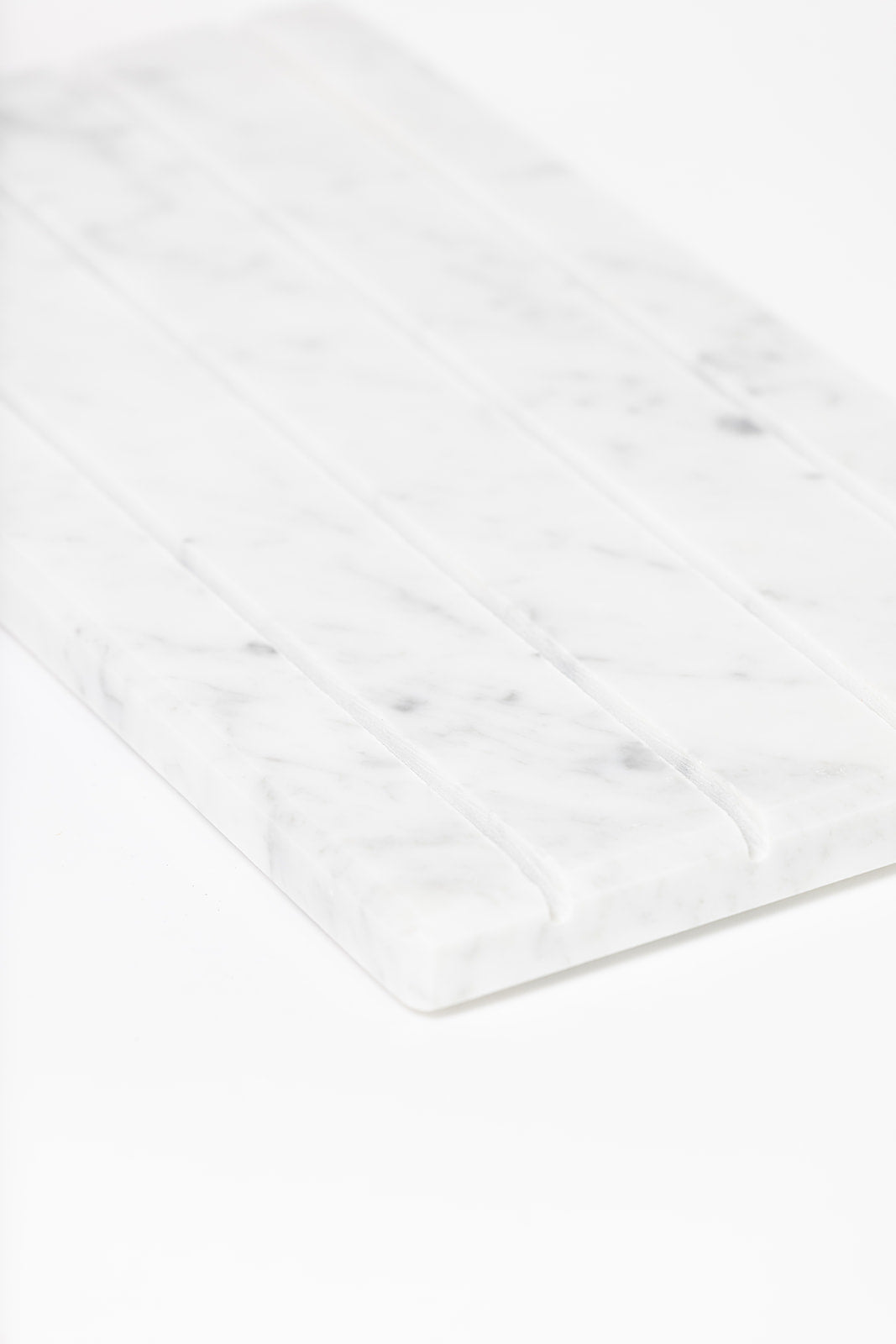 Detail of a grooved white Marble Tray DISPLAY at an angle, showing the smooth polished edge and grey veining.
