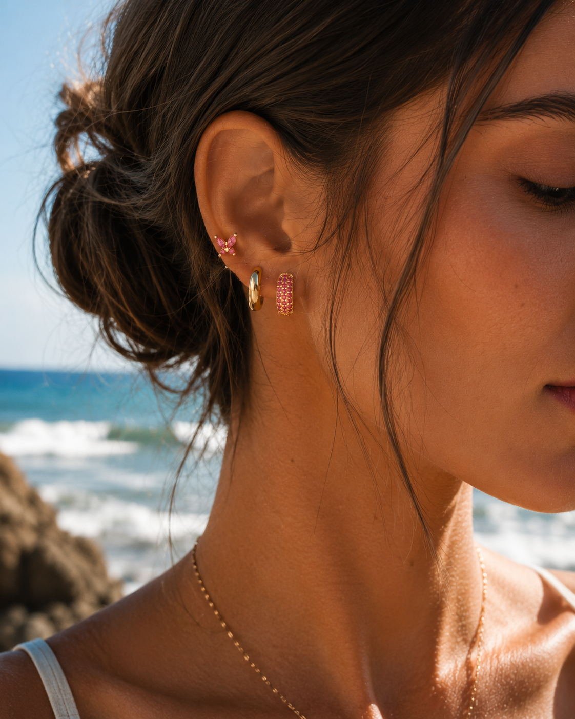 A model wears the three-piece Marigold SET gold earrings in pink stacked along her ear, including a pave hoop.