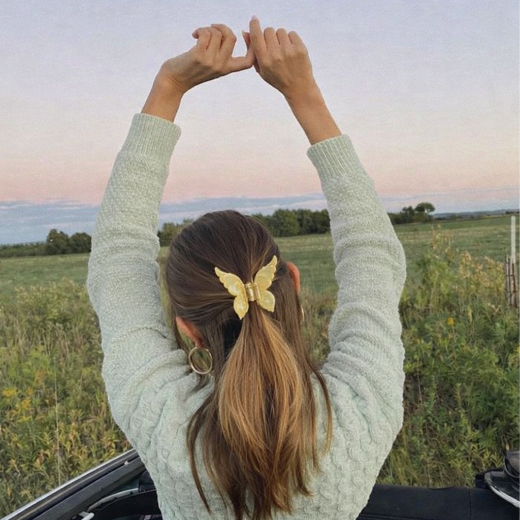 Mariposa HAIR CLIP's golden butterfly clip worn in a ponytail outdoors, photographed against a sunset field.