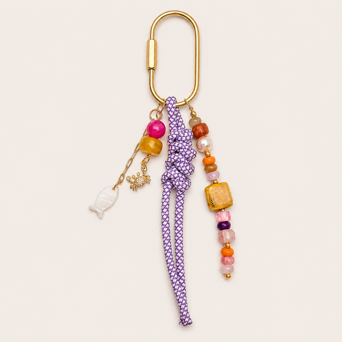 Folie à Trois Marisol BAG CHARM, a purple rope tassel with colorful beaded strands and gold fish and crab charms, on a gold carabiner clasp.