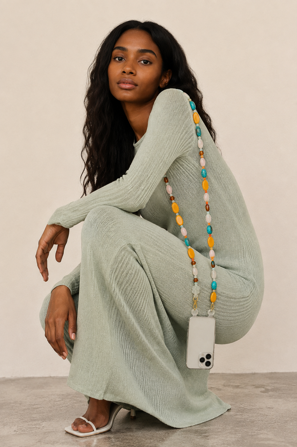 Woman in a sage green knit set crouches with a colourful beaded phone chain clipped to her phone — Folie à Trois Marisol long phone chain