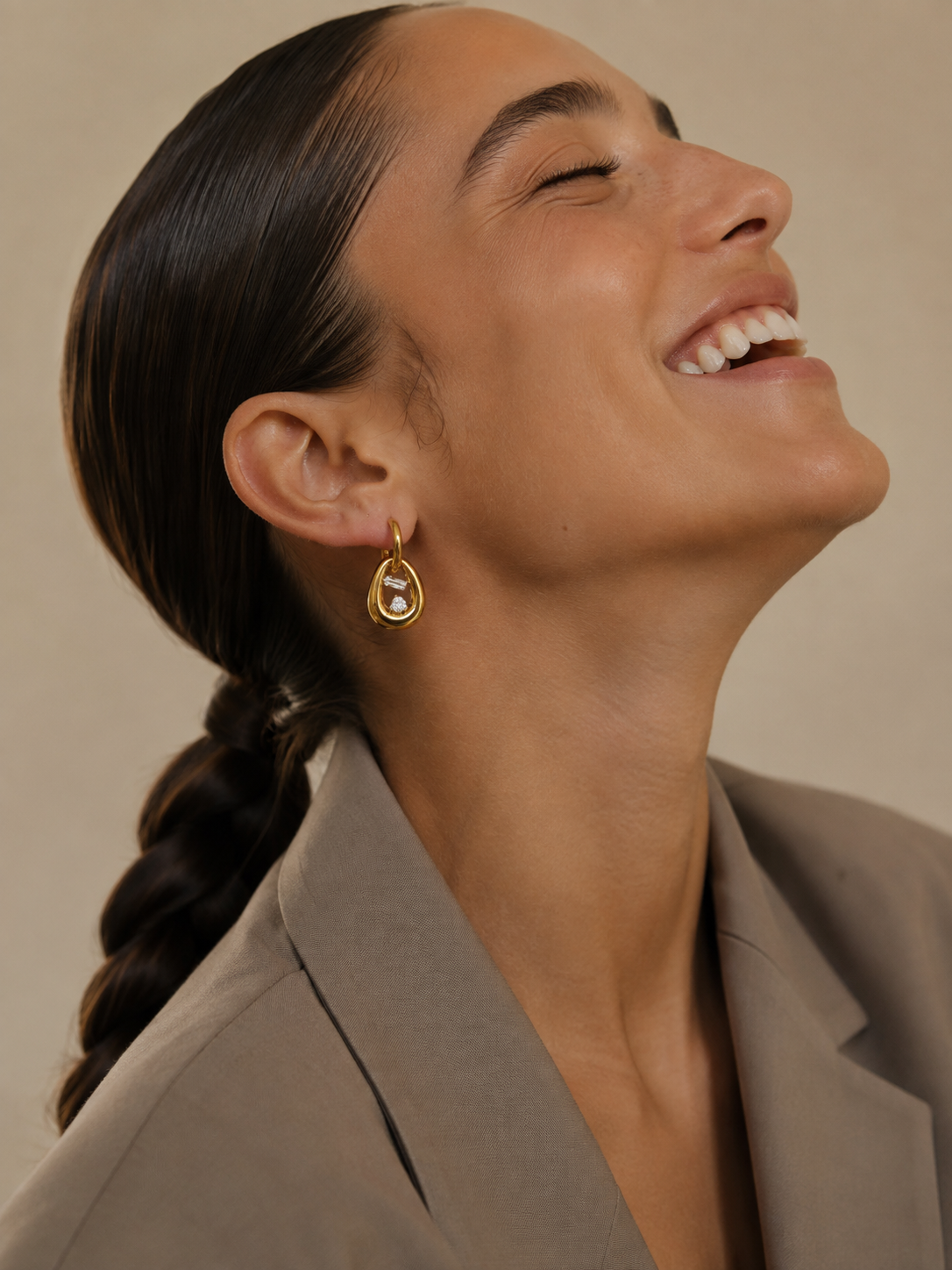 Model wears the gold Folie à Trois Marnie EARRINGS, an oval link drop with a baguette zirconia stone, styled with a tailored blazer.