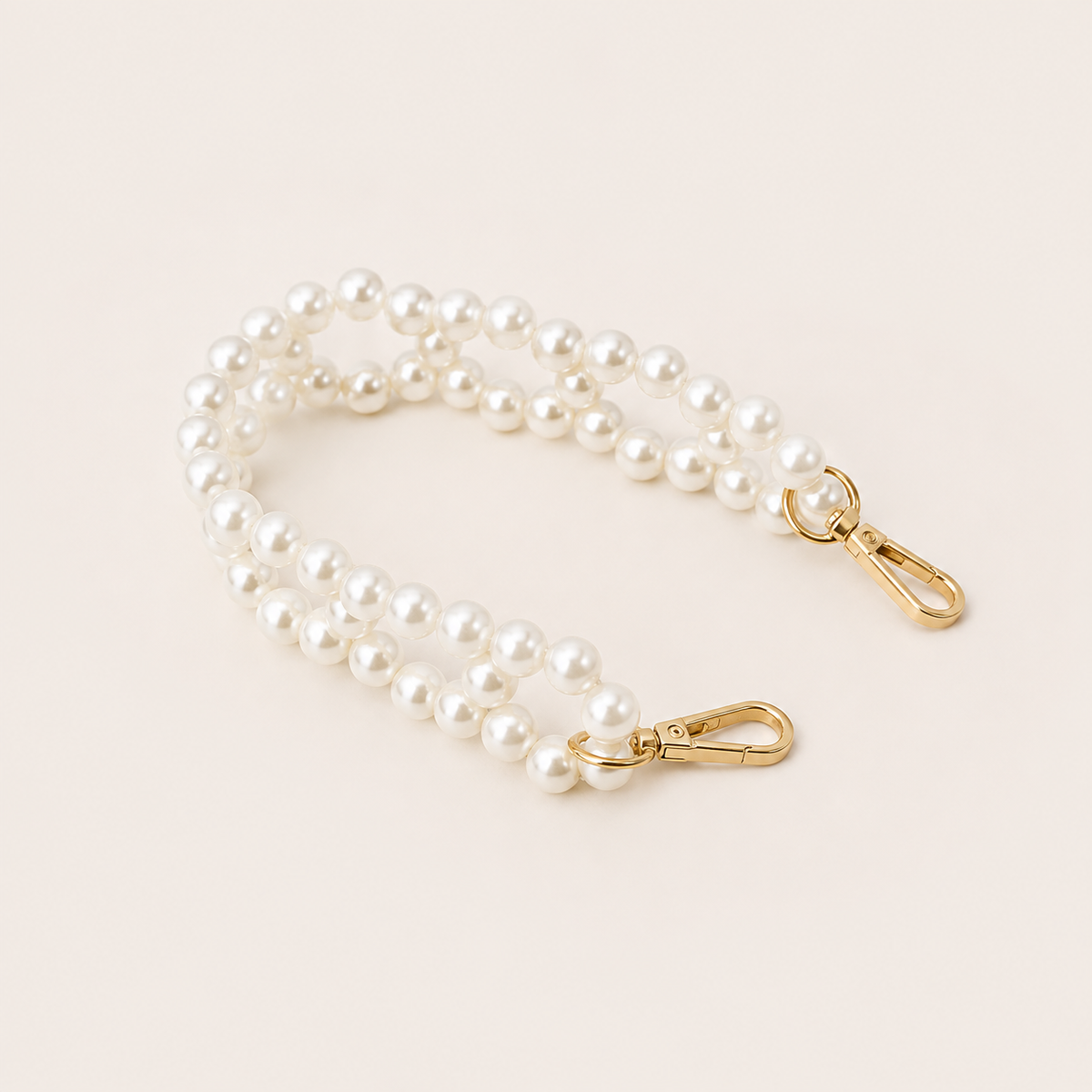 Folie à Trois Marnie Pearl short phone chain in a double strand of white faux pearls with gold clasps, coiled on a cream background.