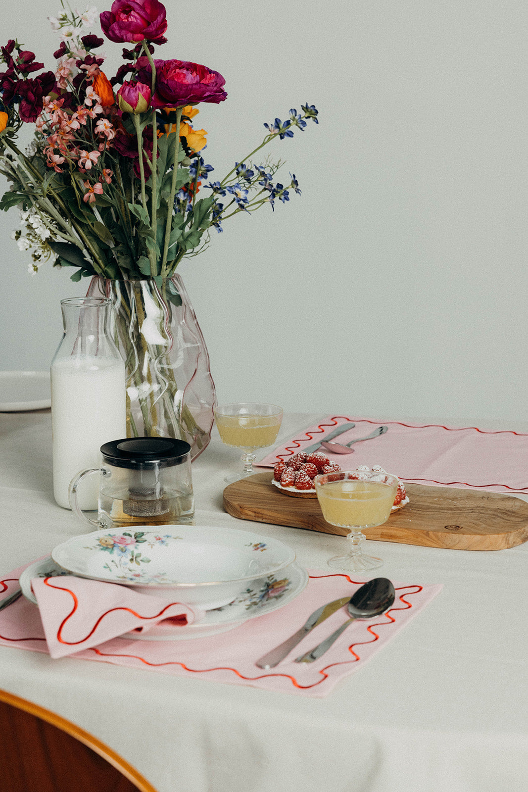 Khaki Maude wave-trim placemat set with white stacked plates, a coffee cup, fresh artichokes and lemons on linen.