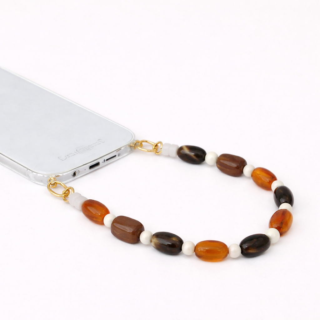 Brown, orange, and black stone-bead Meryn SHORT PHONE STRAP clipped to a clear phone case with gold hardware.