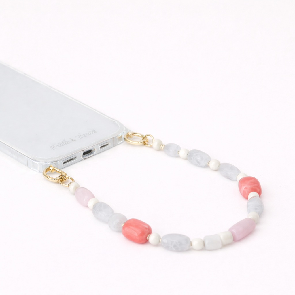 Gray, pink, and coral beaded Meryn SHORT PHONE STRAP clipped to a clear phone case with gold hardware.