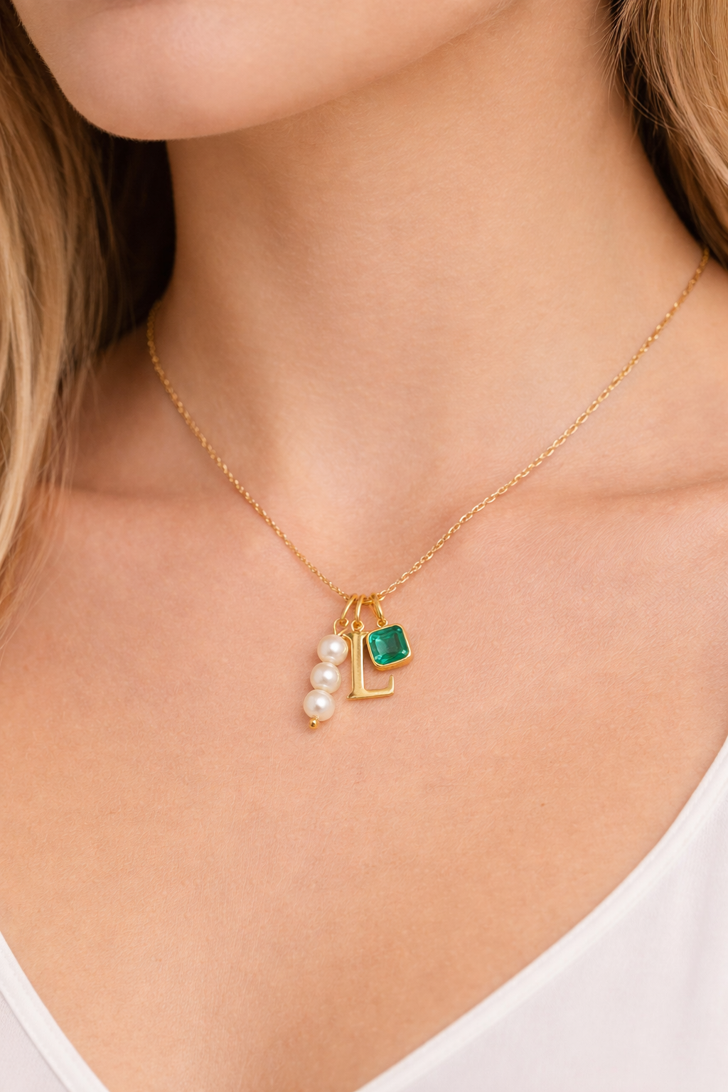 The Minimal NECKLACE worn at the neckline with a gold L initial charm, pearl beads, and a square emerald charm attached.