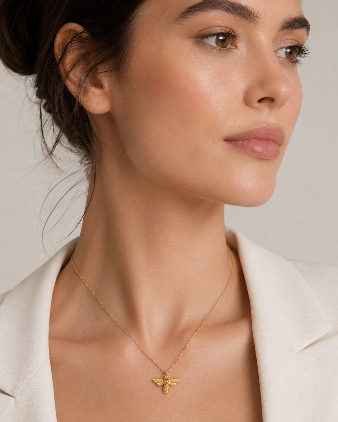 The Minimal NECKLACE worn at the neckline with a small gold winged insect charm attached, cream blazer in the background.