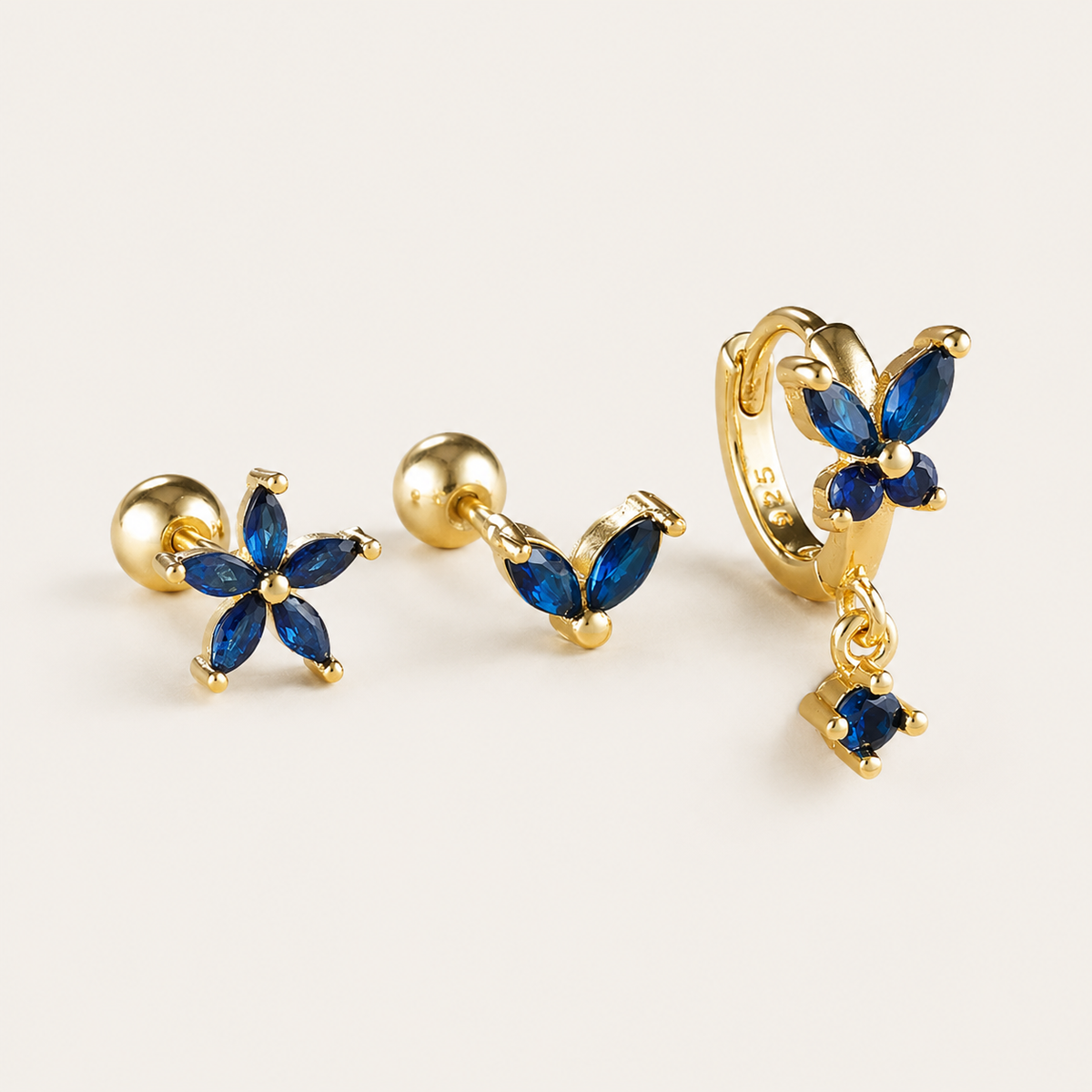 Three-piece Misha SET gold earrings in blue: a flower stud, a small V-shaped stud, and a flower hoop with a drop charm.