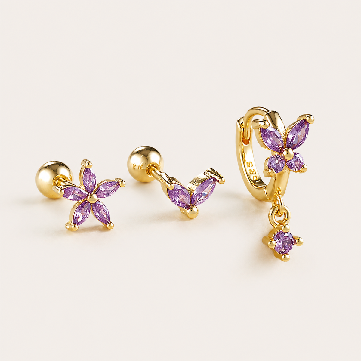 Three-piece Misha SET gold earrings in purple: a flower stud, a small V-shaped stud, and a flower hoop with a drop charm.