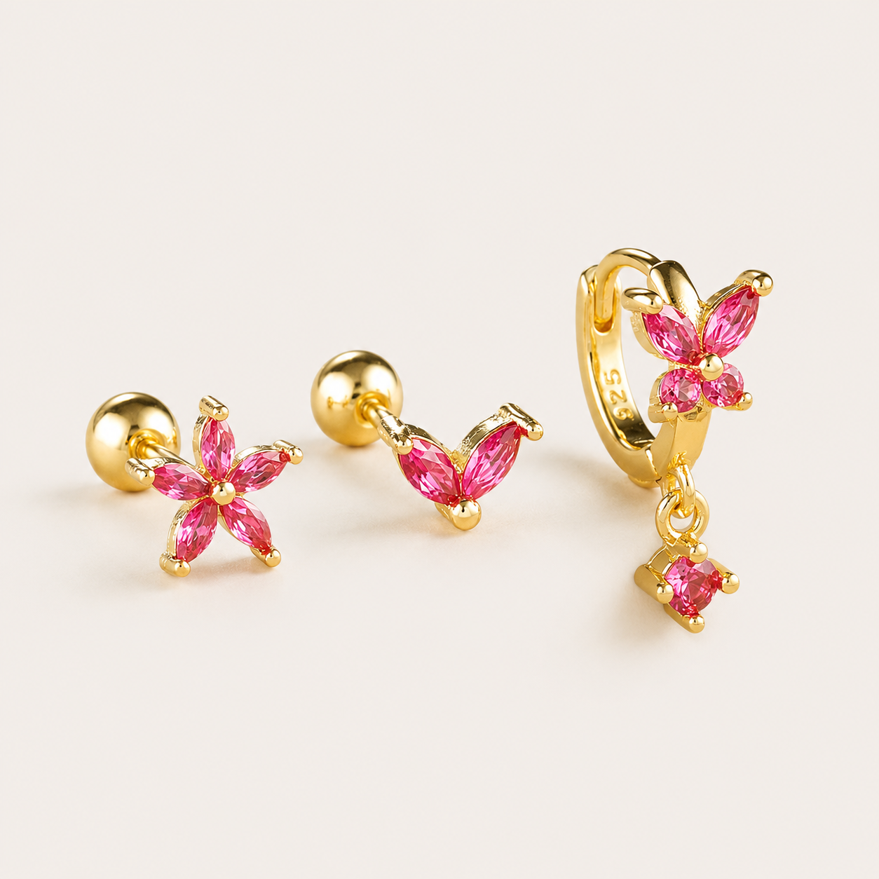 Three-piece Misha SET gold earrings in pink: a flower stud, a small V-shaped stud, and a flower hoop with a drop charm.