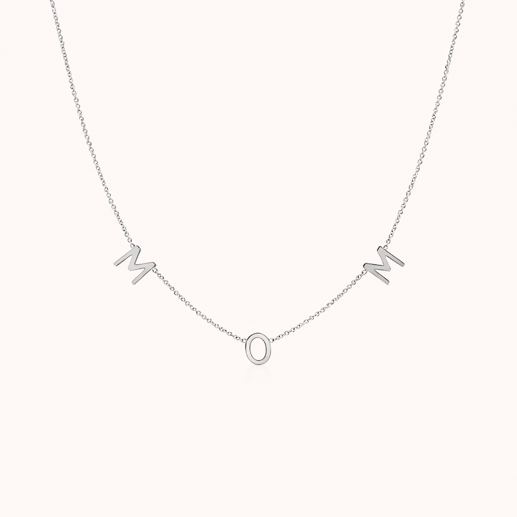 The Mom NECKLACE in silver, individual letters spelling MOM dangling from a fine chain, shown on a cream background.