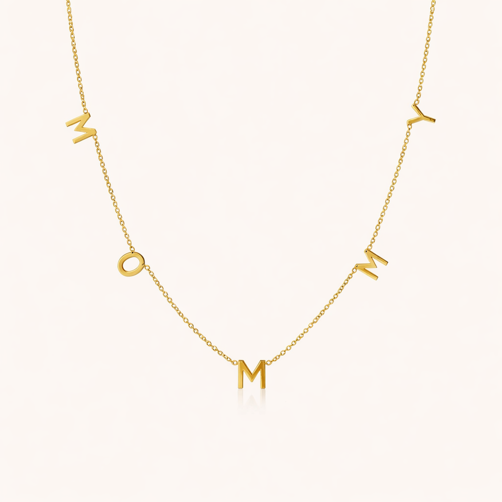 The Mommy NECKLACE in gold, individual letters spelling MOMMY dangling from a fine chain, shown on a cream background.