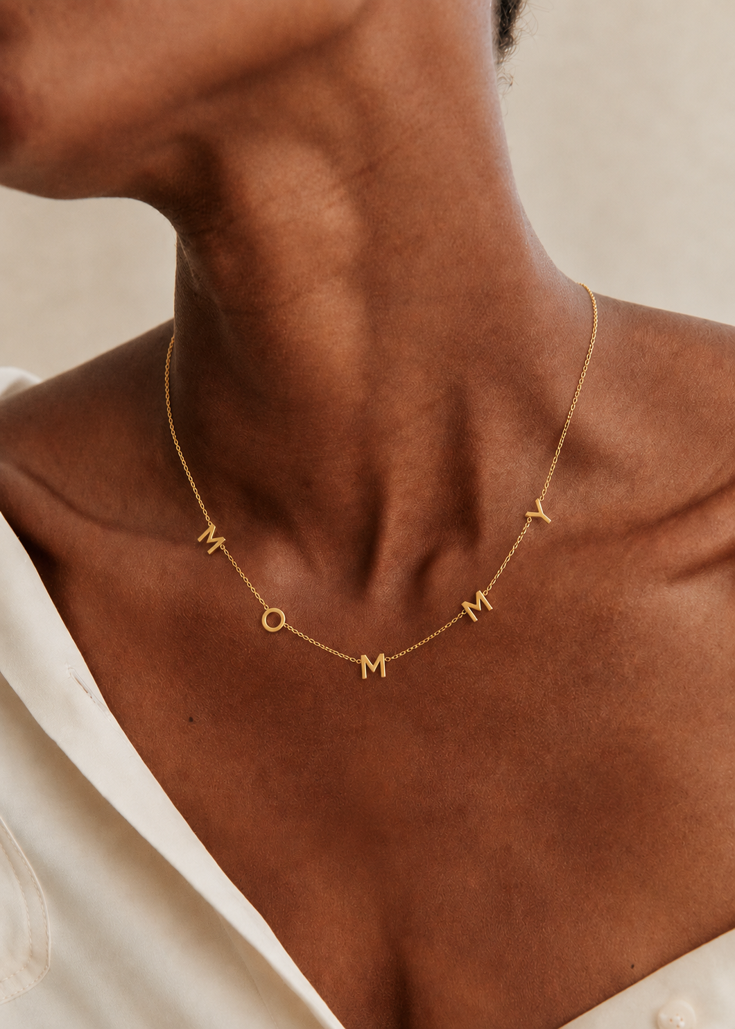 The Mommy NECKLACE in gold worn at the neckline, individual gold letters spelling MOMMY on a fine chain.