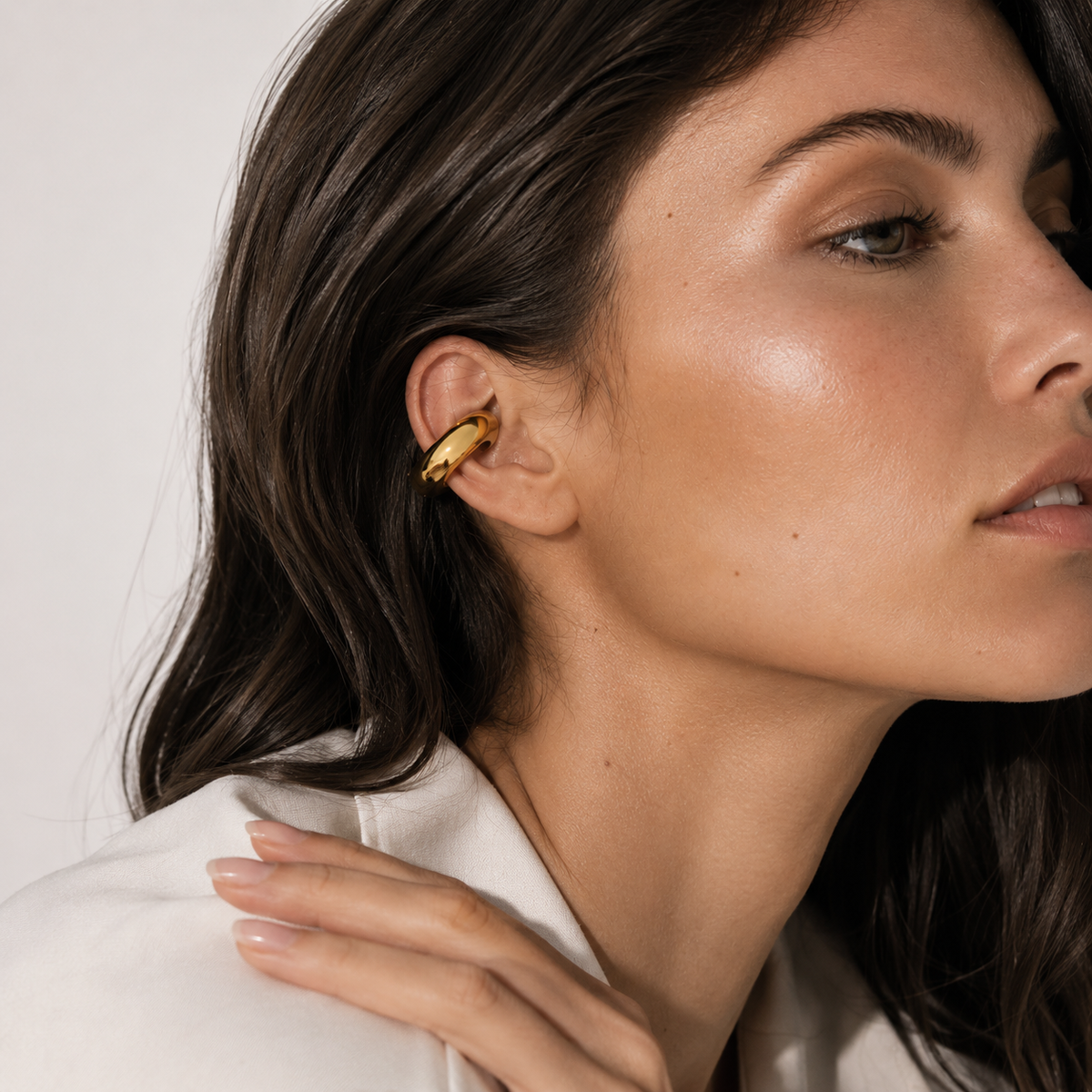The Moon EAR CUFF worn on the ear cartilage in close-up, a smooth gold tube cuff shown against soft light.