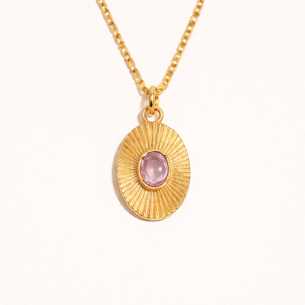 The More Than Friends NECKLACE in gold with a pink stone, a sunburst-textured oval pendant on a fine chain, shown flat.