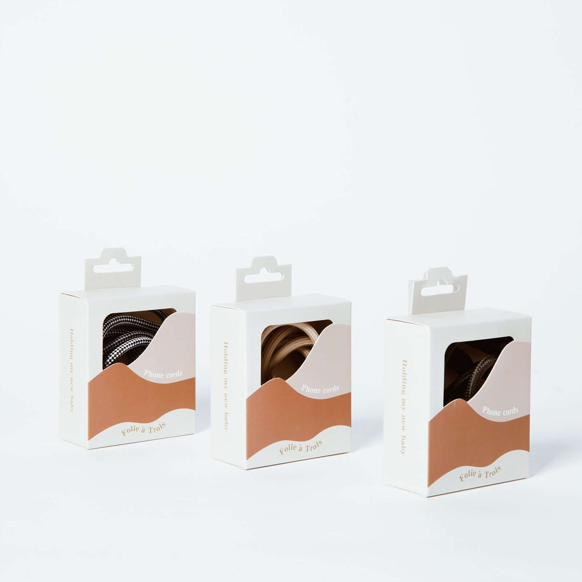 Three Multi Colorful PHONE CORD packaging boxes by Folie à Trois, showing black-and-white, beige and patterned cords.