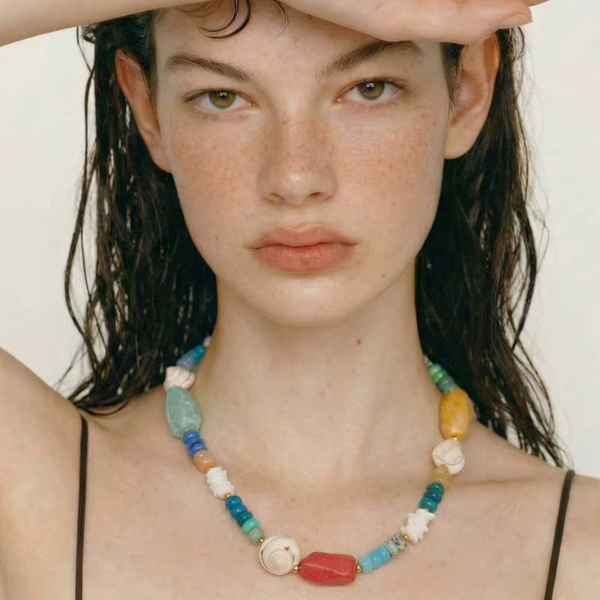 The Mykonos NECKLACE worn close-up as the model shields her eyes, its multicolor gemstone and shell beads on full display.