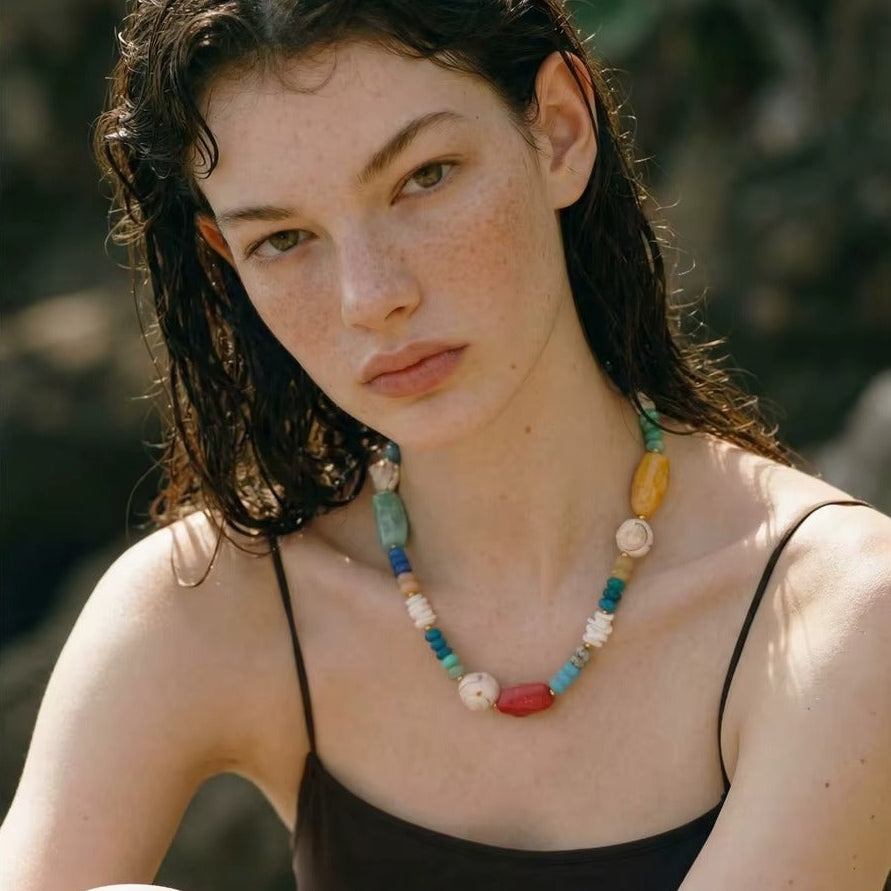 The Mykonos NECKLACE worn close-up outdoors, the model gazing to the side with wet hair and a dark strappy top.