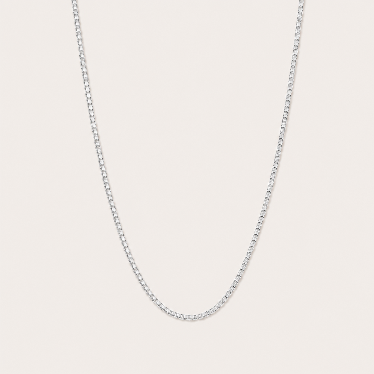 Silver box-chain necklace with a fine square-link design, the Nara NECKLACE, shown in a close-up studio shot on a beige background.