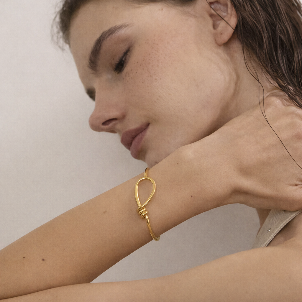 Neeve BRACELET worn in gold on the wrist, model resting her chin on her arm with damp hair.