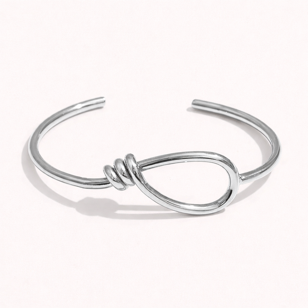 Neeve BRACELET in silver, open cuff with a knotted teardrop loop detail, studio flat-lay on white.
