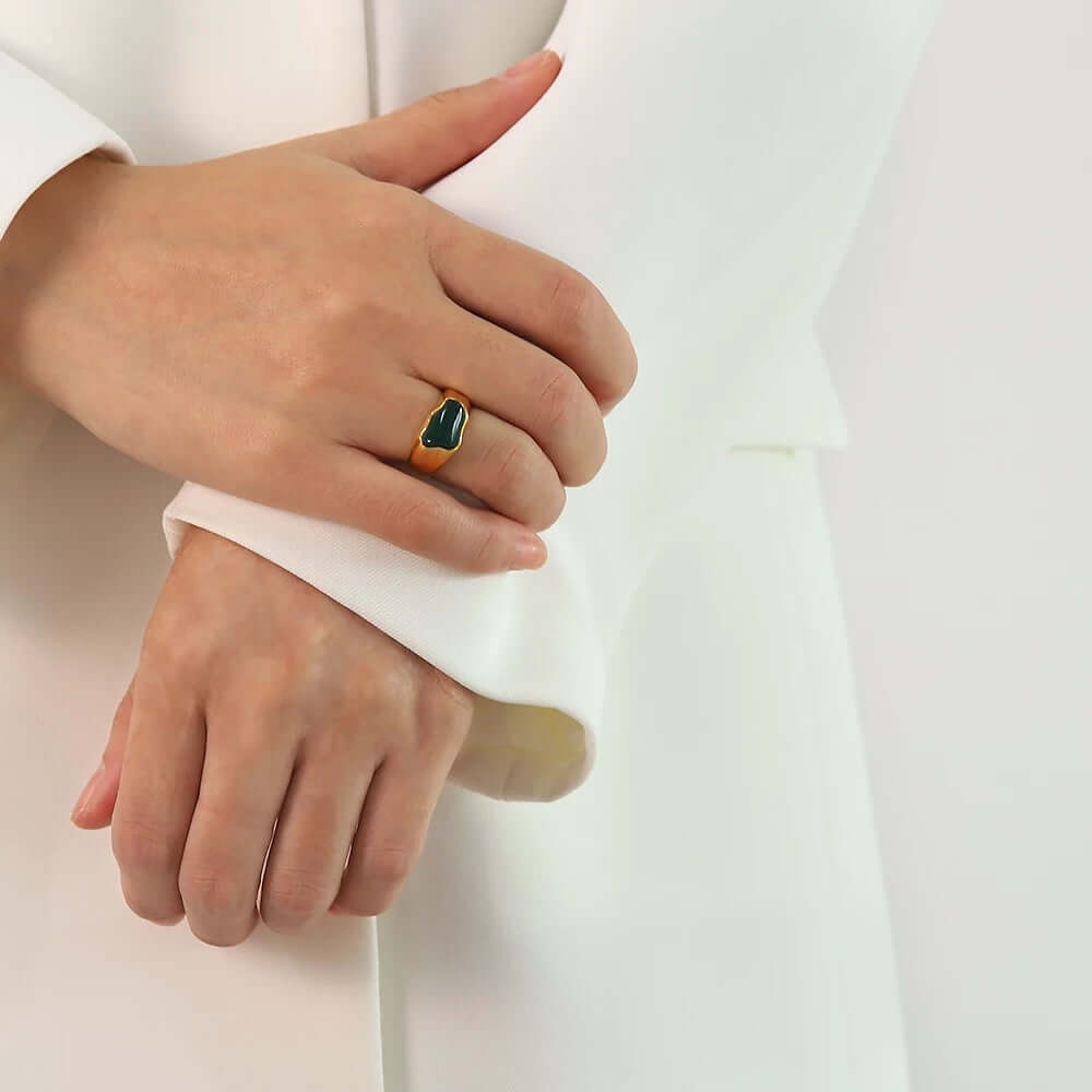 Close-up of a hand with arms crossed wearing the gold signet-style New Fashion RING set with a green cabochon stone.