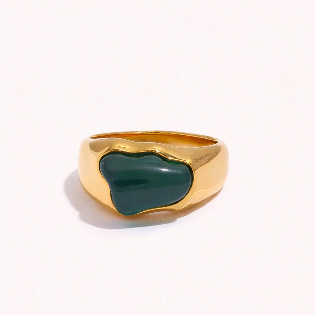 Gold signet-style New Fashion RING set with an irregular green cabochon stone, shown at an angle on a cream backdrop.