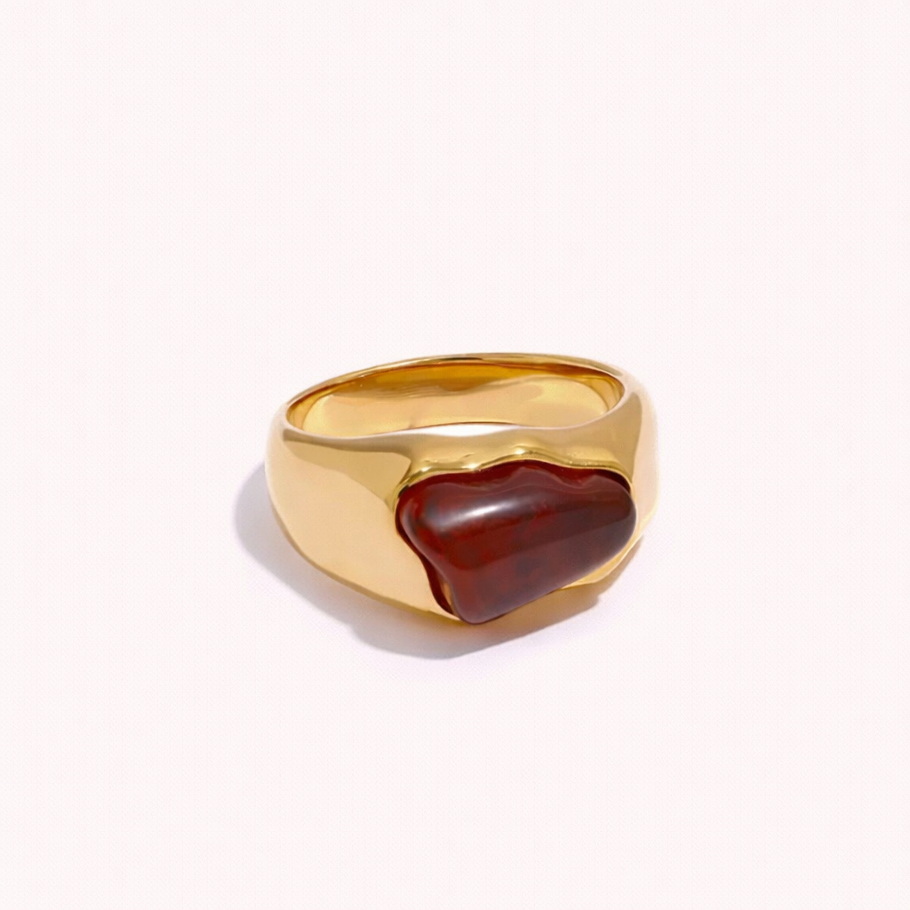 Gold signet-style New Fashion RING set with an irregular amber cabochon stone, shown at an angle on a cream backdrop.