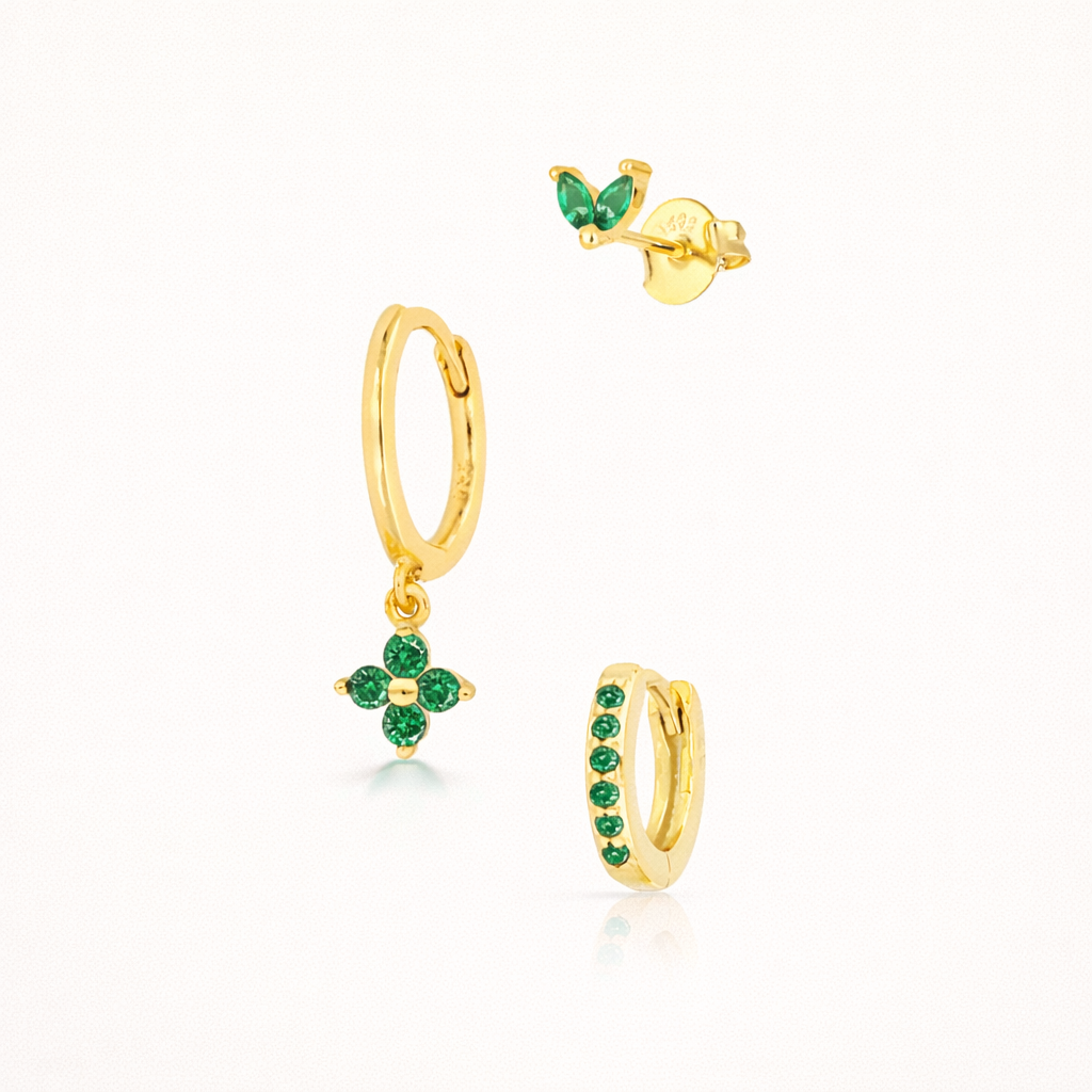 The New Perspective SET in gold with emerald green stones, featuring a marquise stud, flower dangle hoop, and pavé hoop in a studio shot.