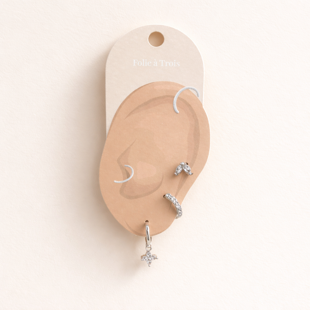 The New Perspective SET in silver displayed on a branded Folie à Trois ear card with the marquise stud, pavé hoop, and flower dangle hoop.