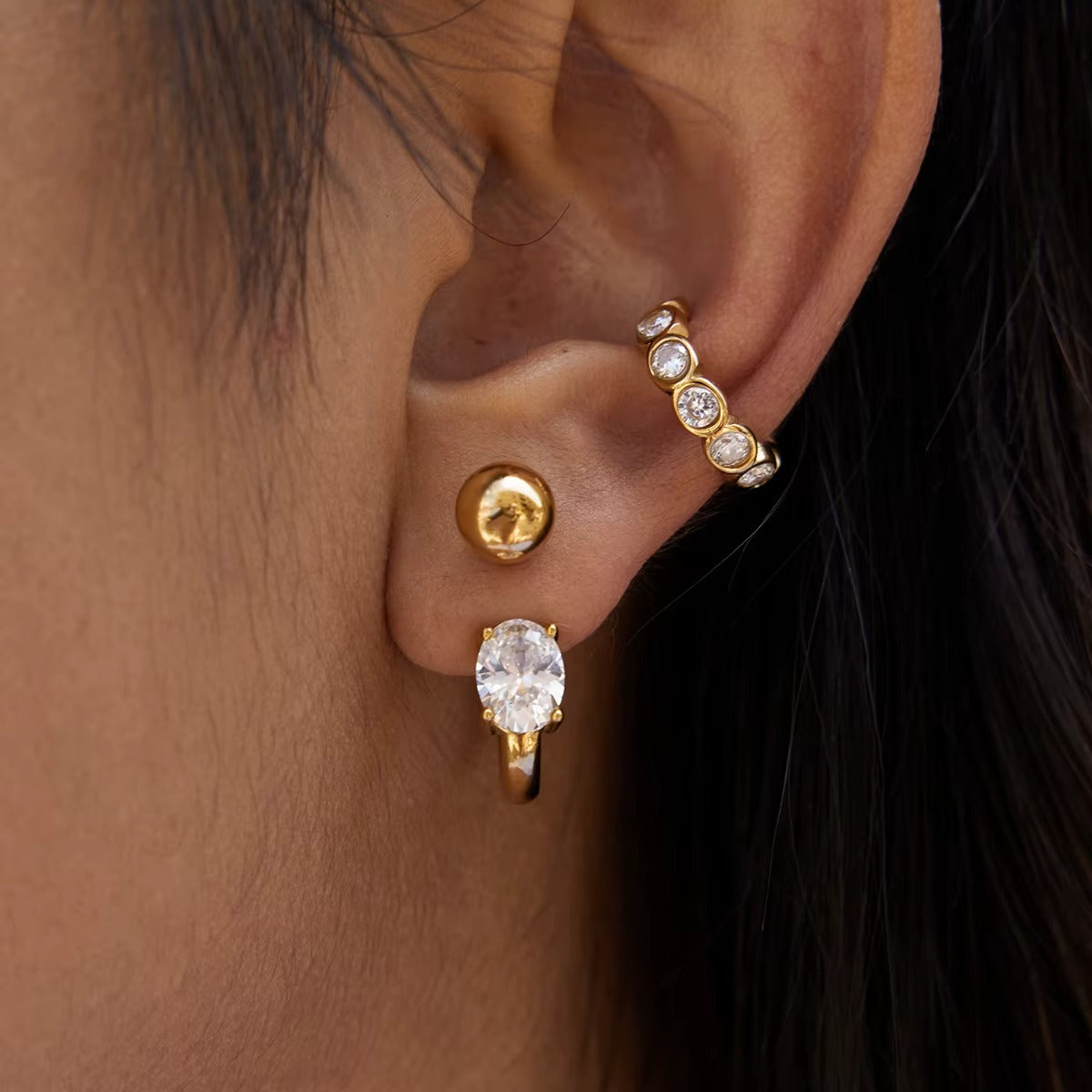 Close-up of the Nomad ear cuff worn on the upper ear, showing the bezel-set crystals beside a ball stud and oval crystal earring.