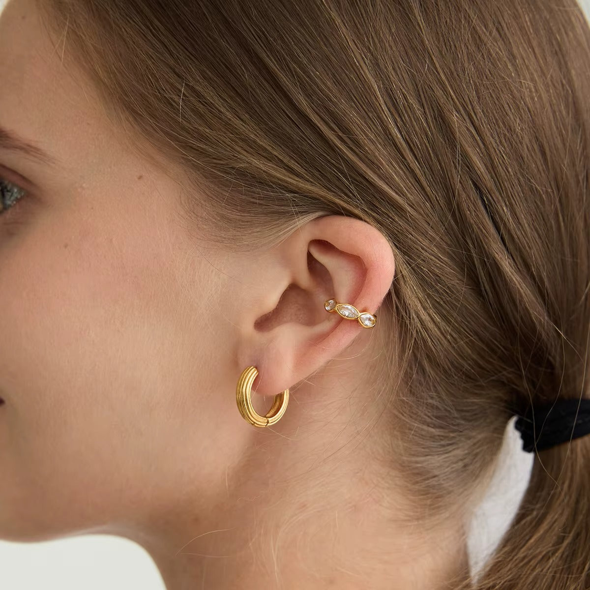 Overdrive ear cuff worn on the cartilage with marquise crystals catching the light above a ribbed gold hoop earring.
