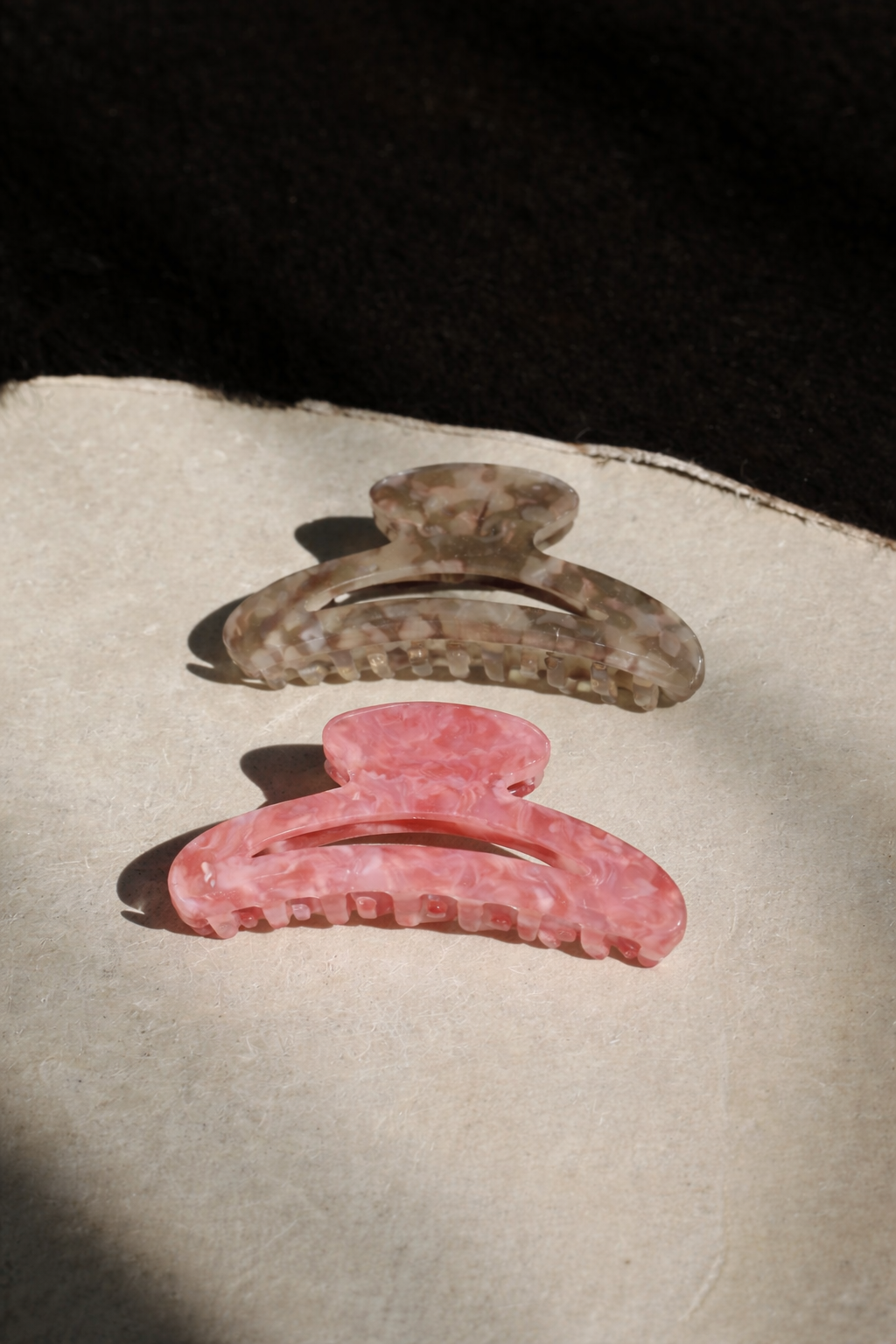 Palm Springs HAIR CLIP's grey and pink marbled claw clips laid on a paper card in sunlight.